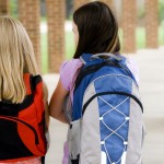 Two young girls carrying their book bags
